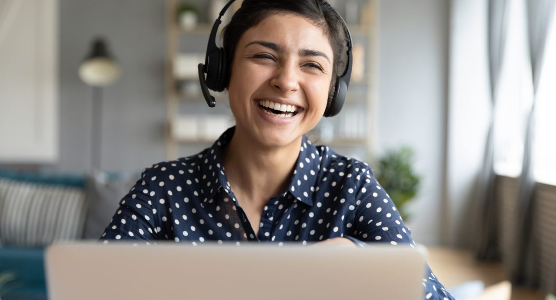 Cheerful indian woman wear headset laugh using laptop video stream conference call teach online, happy ethnic girl student gamer tutor have fun watch webinar web cam education entertainment concept